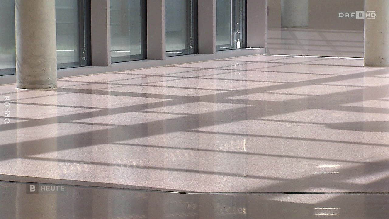 Ein Innenbereich mit Glaswänden und einem glänzenden weißen Boden, der Licht und Schatten reflektiert.