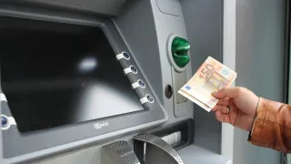 Eine Person steckt einen 50-Euro-Schein in einen Geldautomaten. Der Geldautomat ist grau mit einem großen Bildschirm und Tasten.