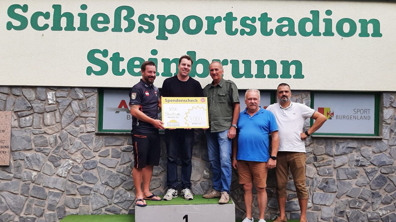 Fünf Männer stehen vor einer Wand mit dem Text 'Steinborn Sportstadion'. Ein Mann hält einen Scheck über 1.500 Euro. Sie alle lächeln und scheinen zu feiern.