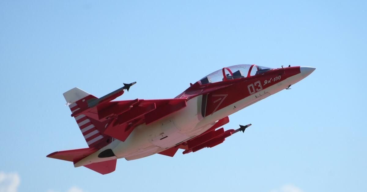 Ein rot-weißes Kampfflugzeug mit der Nummer 03 und den Buchstaben 9K-130 fliegt am Himmel.