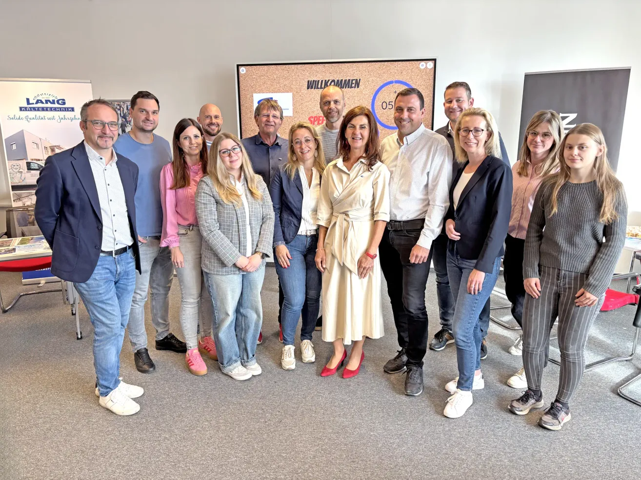 Eine Gruppe von Menschen in Geschäftskleidung steht vor einem Schild mit dem Wort willkommen. Sie lächeln und posieren für ein Foto.