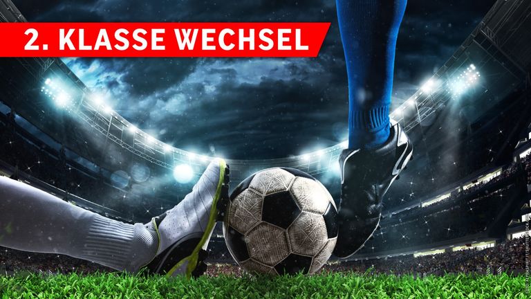 Ein Fußballspieler tritt einen Ball mit dem Text 'SSE WECHSEL' auf einem roten Banner. Der Spieler trägt blaue Socken und schwarze Stollenschuhe. Der Hintergrund zeigt ein Stadion mit bewölktem Himmel.