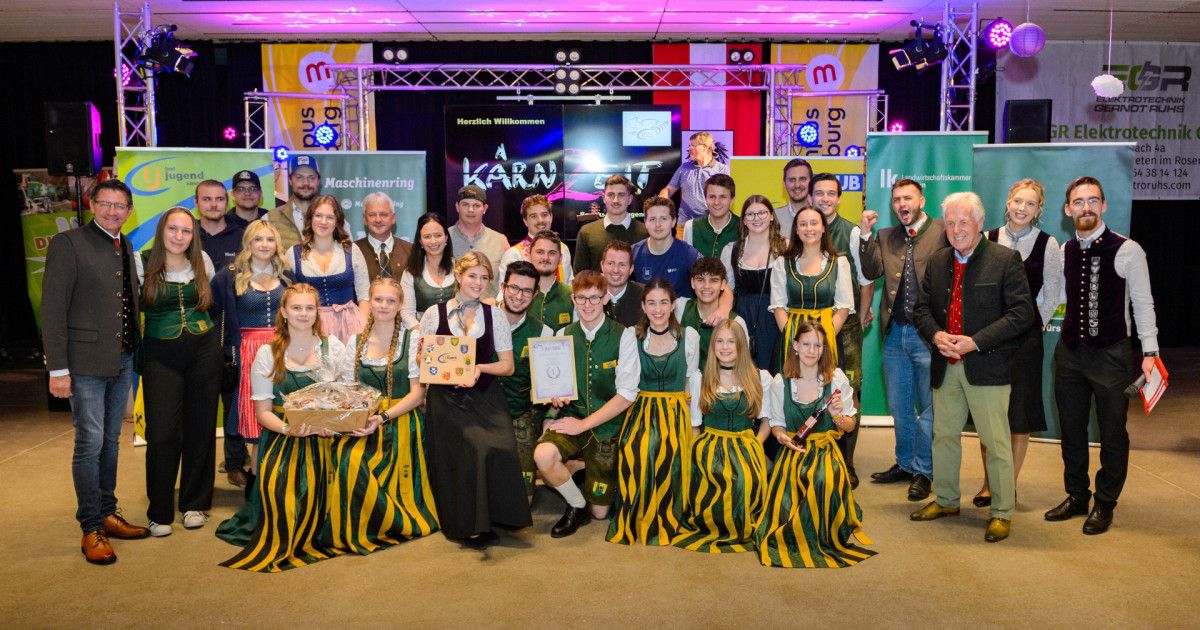 Eine Gruppe von Personen in traditioneller Kleidung posiert für ein Foto auf der Bühne mit einem Schild, das 'A KARN 17' liest.