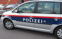 Ein silberner Polizeiwagen mit roten und blauen Streifen steht am Straßenrand. Das Wort 'POLIZEI' ist in Weiß auf der Seite des Wagens geschrieben.