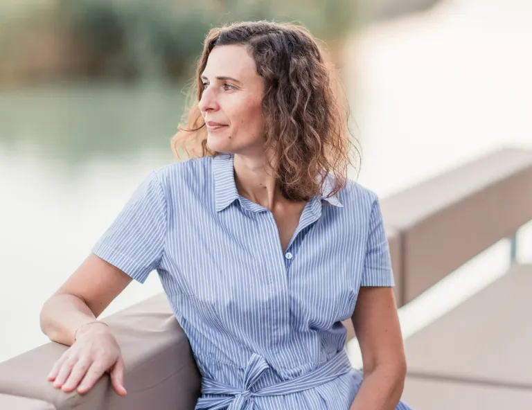 A woman with curly hair and a blue striped shirt is sitting on a couch, looking to the left.