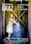 Ein Mädchen in einem bunten Kleid steht in einem Stall und spritzt Wasser auf ihre Hände. Der Stall ist aus Holz, und der Text darüber lautet 'GRAZ' und 'SCHOCKL ST. RADEGUND'.
