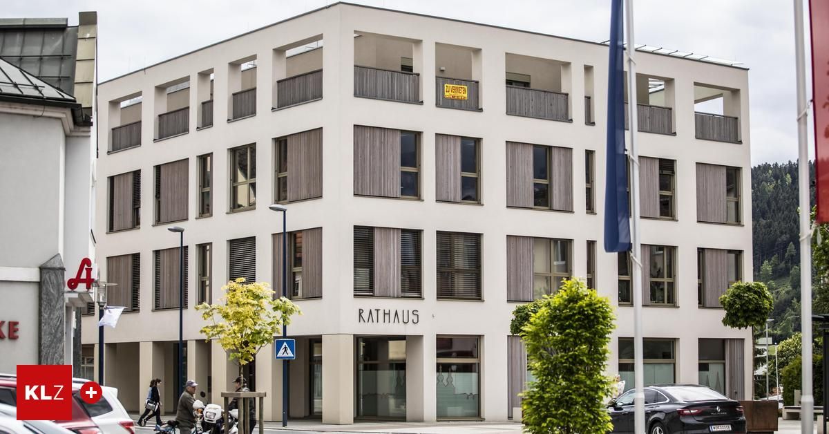 Ein modernes Gebäude mit mehreren Stockwerken, beschriftet mit Rathaus. Vor dem Gebäude gehen zwei Personen, und ein Auto ist in der Nähe geparkt.