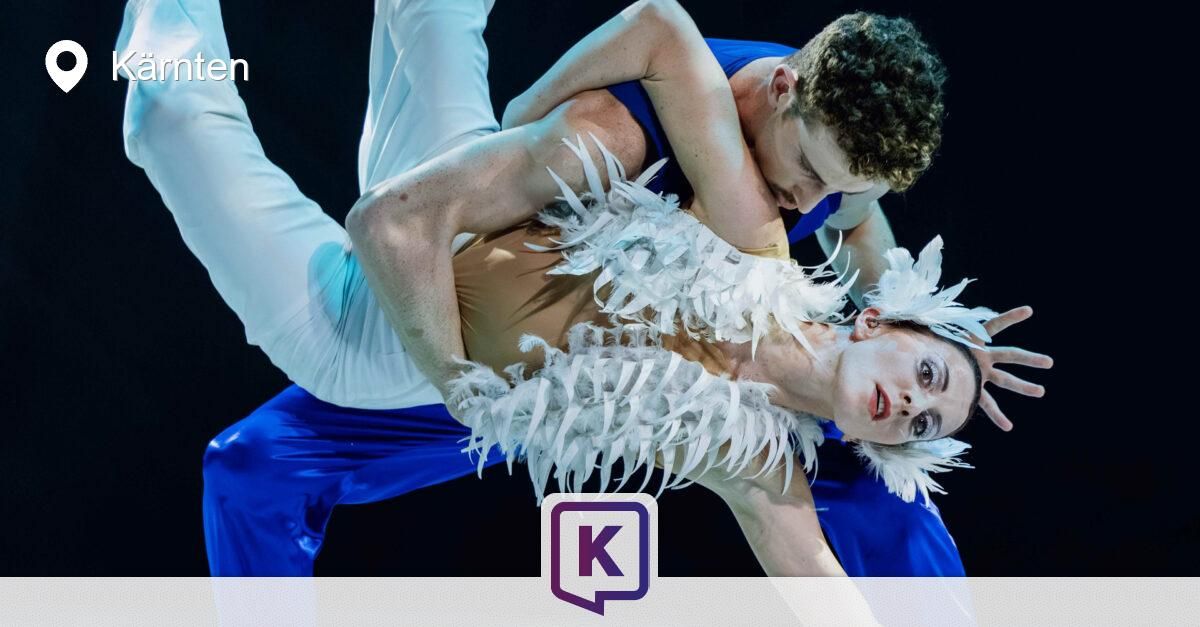 Ein Mann und eine Frau führen eine Tanzroutine auf, wobei der Mann die Taille der Frau hält und sie leicht in die Luft hebt. Sie tragen beide Kostüme mit Federn.