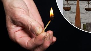 Eine Hand hält einen brennenden Streichholz vor einem Hintergrund aus einer hölzernen Waage und einer Ziegelwand.