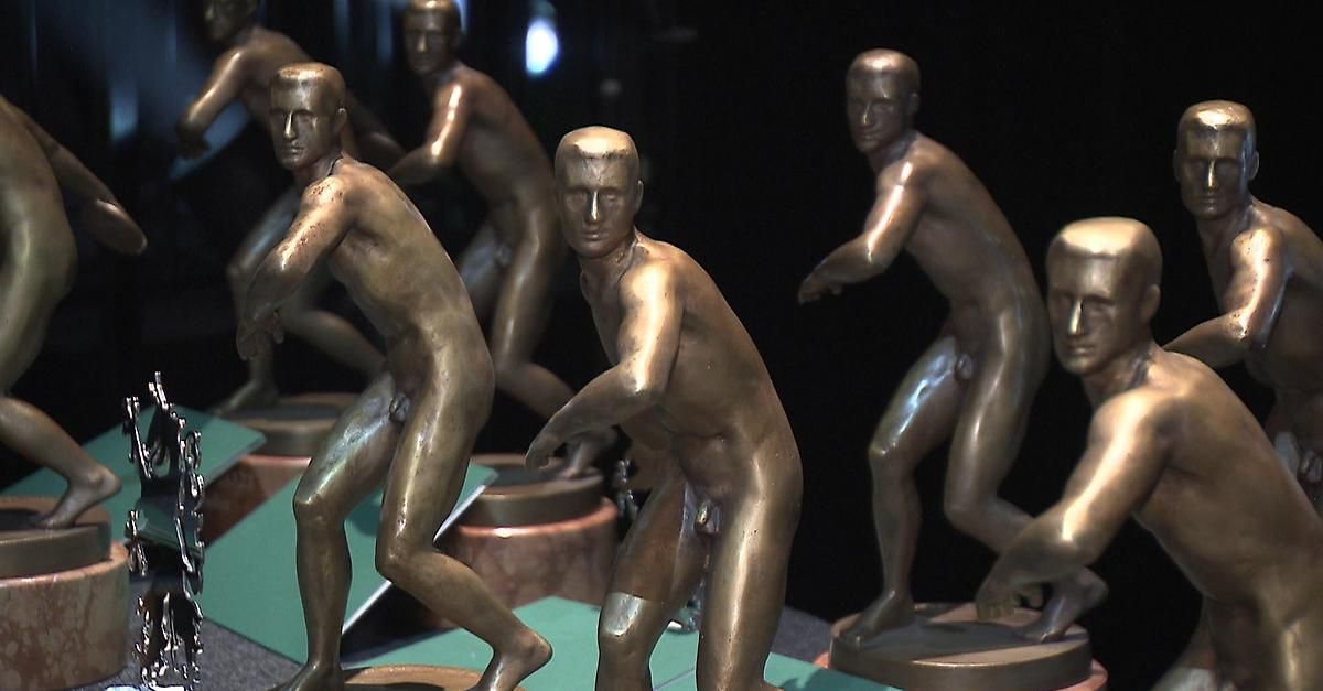 Mehrere bronzene Athletenstatuen sind ausgestellt, jede in einer dynamischen Laufpose. Die Statuen stehen auf hölzernen Sockeln, und der Hintergrund ist dunkel.