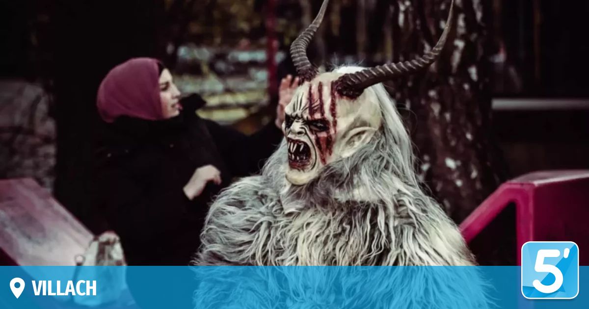 Eine Person mit einer blutverschmierten Hörnermaske nähert sich einer Frau mit einem Hijab. Der Hintergrund ist unscharf mit Bäumen und Strukturen.