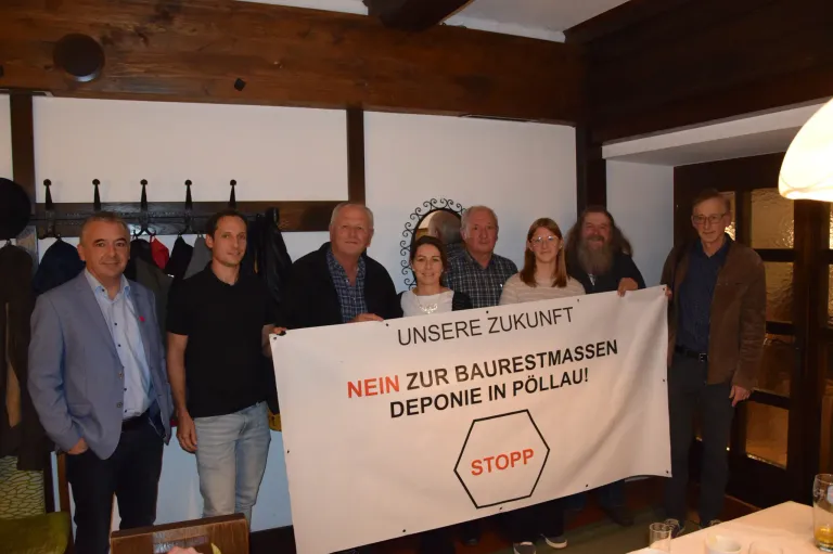 Eine Gruppe von Menschen steht hinter einem weißen Banner mit rotem Text und protestiert gegen die Mülldeponie in Pollau. Sie halten das Banner mit beiden Händen.