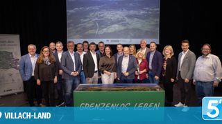 Eine Gruppe von Menschen steht zusammen mit einem Hintergrund einer Präsentation und einer Landschaft. Das Schild sagt 'Grenzlos Leben'.