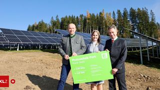 Drei Personen stehen vor einem Solarpark mit einem grünen Schild, das Photovoltaik-Park Prank Stelli zeigt und ein neues Energieprojekt präsentiert.