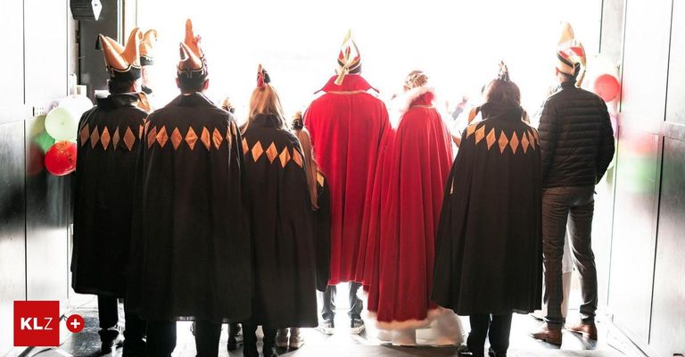 Eine Gruppe von Menschen in Kostümen, einige mit roten Umhängen und andere mit schwarzen Umhängen, stehen in einer Reihe und blicken in die gleiche Richtung. Sie nehmen wahrscheinlich an einer Parade teil.