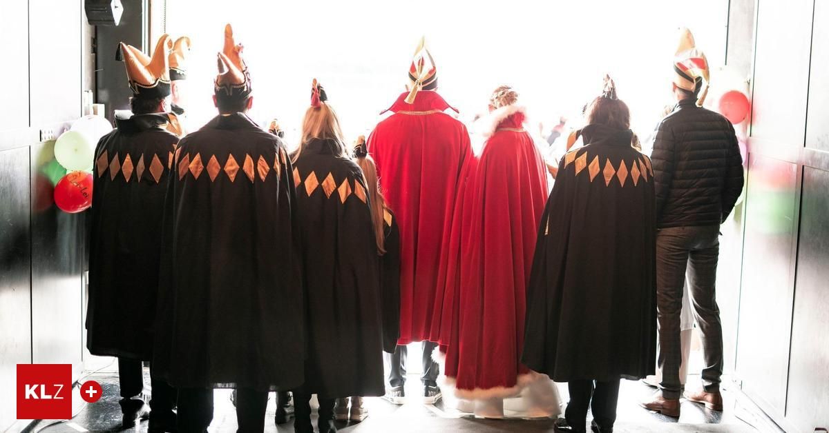 Eine Gruppe von Menschen in Kostümen, einige mit roten Umhängen und andere mit schwarzen Umhängen, stehen in einer Reihe und blicken in die gleiche Richtung. Sie nehmen wahrscheinlich an einer Parade teil.