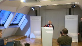 Eine Frau steht an einem Rednerpult mit Mikrofonen vor einem Hintergrund mit der Aufschrift 'Bundesministerium für Arbeit, Soziales, Gesundheit und Verbraucherschutz'. Dahinter hält ein Fotograf den Moment fest.