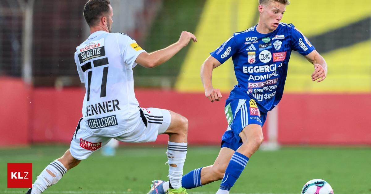 Zwei Fußballspieler rennen auf dem Feld, einer trägt ein weißes Trikot mit der Nummer 11 und der andere ein blaues Trikot mit verschiedenen Werbeaufdrucken.