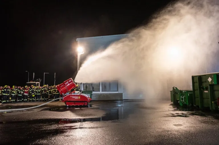 A fire truck sprays water into a building at night. Firefighters are standing nearby.