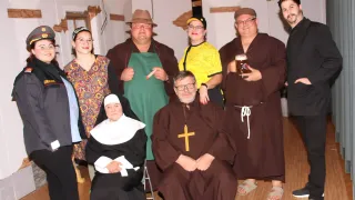 Eine Gruppe von Erwachsenen in Kostümen posiert für ein Foto. Eine Nonne, ein Mönch und eine Person in einem gelben T-Shirt sind anwesend. Ein anderer Mann hält ein Bierglas.