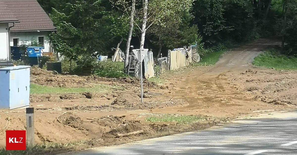 Eine schlammige Straße mit Schmutz und Trümmern, einem Pfosten in der Mitte und mehreren Bäumen und Sträuchern an der Seite. Es gibt auch einige Gegenstände wie Leitern und Planen.