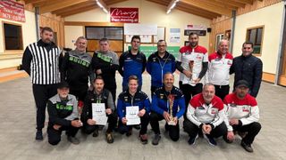 Eine Gruppe von Männern in Sportbekleidung hält Pokale und Urkunden. Sie lächeln und posieren für ein Foto in einer Sporthalle.