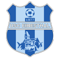 Das Emblem des USC Eibestal, gegründet 1977, zeigt einen blau-weißen Schild mit einem Fußball in der Mitte und einem Gebäude darunter.