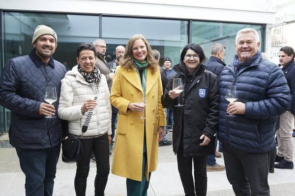 Eine Gruppe lächelnder Menschen steht vor einem Gebäude und hält Wein glasses in der Hand, wahrscheinlich bei einer gesellschaftlichen Veranstaltung.
