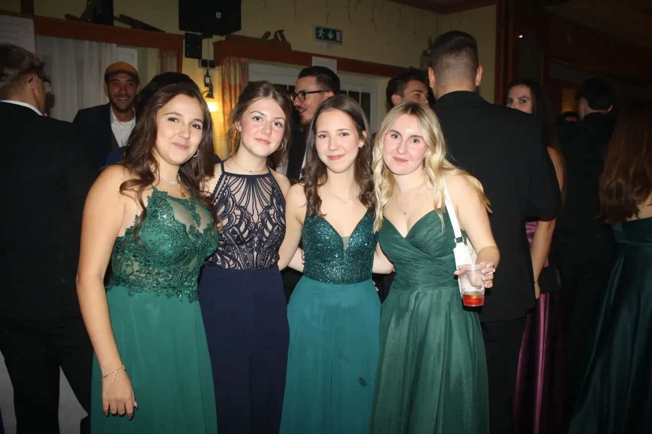 Vier Frauen stehen bei einer Party zusammen. Sie tragen grüne Kleider und scheinen für ein Foto zu posieren. Ein Mann in einem Anzug steht hinter ihnen.