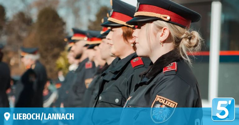 A line of police officers in uniform stand in a row. The officer in front has the word 'POLIZEI' on her shoulder.