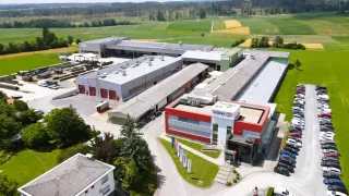 Ein Luftbild einer Fabrik mit einem großen Parkplatz und mehreren Gebäuden, von denen eines den Namen Grobner trägt. Die Fabrik ist von Bäumen und Gras umgeben.
