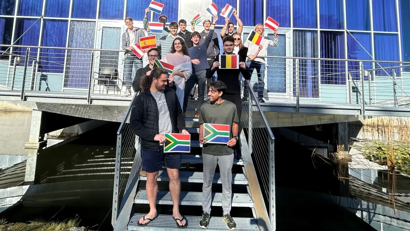 A group of people are standing on a staircase, holding flags from various countries. They are likely posing for a photo.