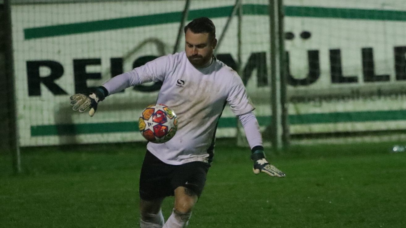 Ein Fußballspieler in einem weißen Trikot tritt einen Ball auf einem grünen Feld.