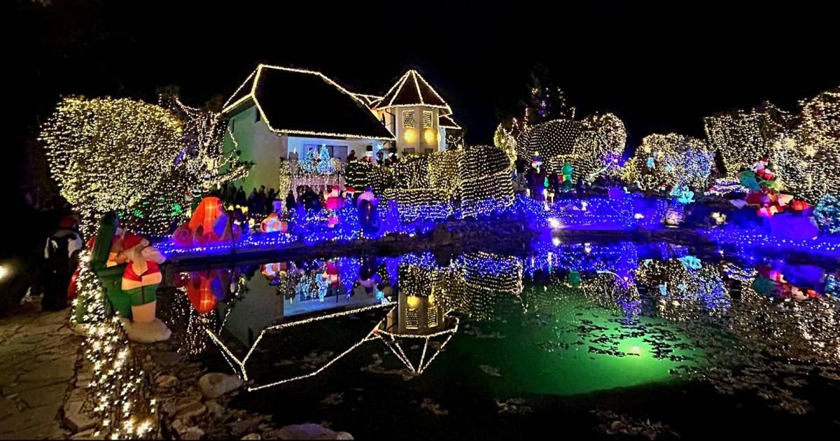 Ein Haus, das mit bunten Lichtern beleuchtet ist, für die Feiertage geschmückt, mit einem Teich, der die Lichter reflektiert, und Menschen, die die festliche Dekoration genießen.