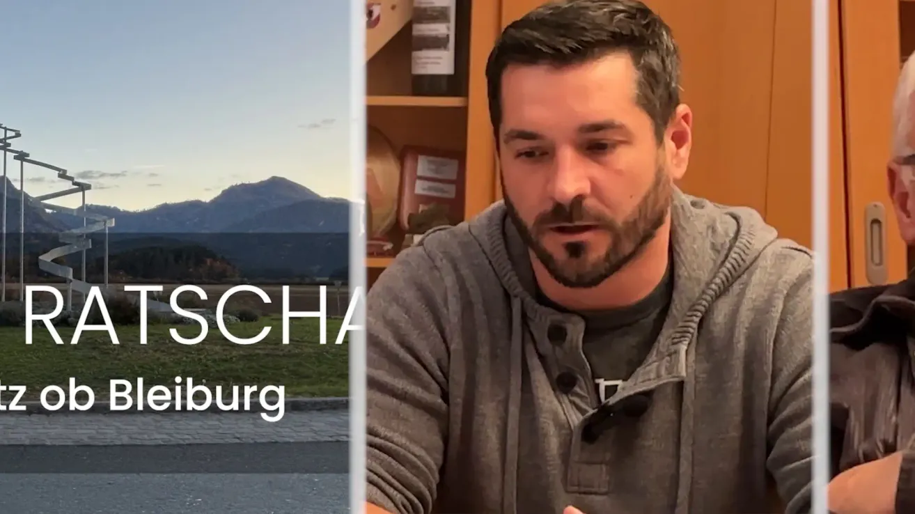 Ein Mann in einer grauen Kapuzenjacke spricht in ein Mikrofon mit einem unscharfen Hintergrund, der ein Grasfeld und Berge zeigt. Die Texte 'SCH' und 'burg' sind auf der linken Seite zu sehen.