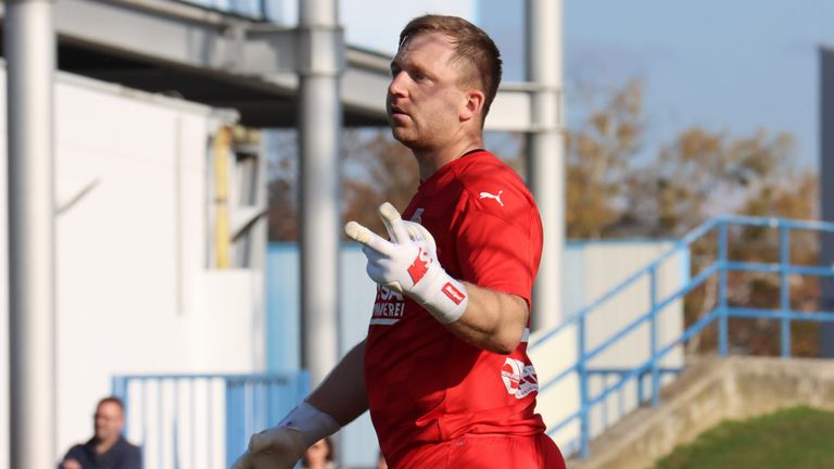 Ein Fußballspieler in einem roten Trikot mit Logo auf der Brust schaut nach links. Er trägt Handschuhe und läuft wahrscheinlich auf dem Feld.