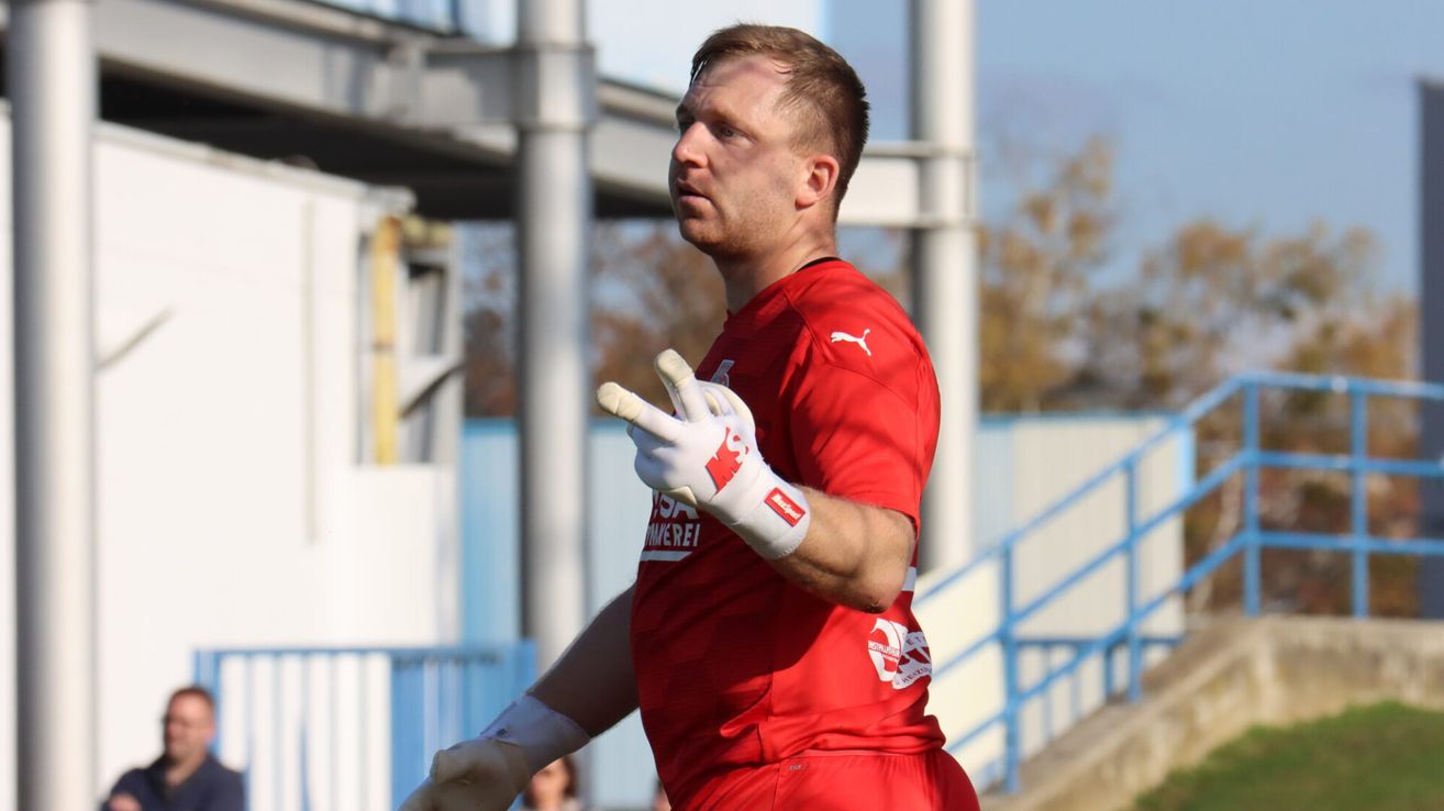 Ein Fußballspieler in einem roten Trikot mit Logo auf der Brust schaut nach links. Er trägt Handschuhe und läuft wahrscheinlich auf dem Feld.