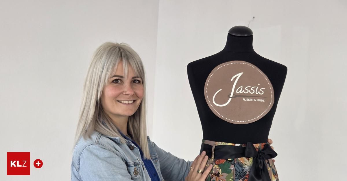 Eine Frau mit blondem Haar steht neben einem Mannequin. Das Mannequin hat ein Etikett mit dem Wort Jassis darauf, zusammen mit einem schwarzen Band. Die Frau lächelt.