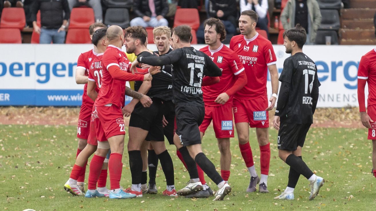 Fußballspieler in roten Trikots feiern, während der Schiedsrichter einen Spieler zurückzieht. Der Spieler trägt ein schwarzes Trikot mit der Nummer 17.