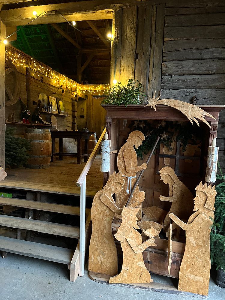 Ein rustikaler Holzraum mit einer Krippe, die hölzerne Figuren von Jesus, Maria, Josef und zwei Hirten zeigt, geschmückt mit Weihnachtsdekoration und einem Stern.