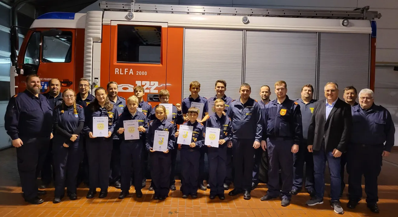 A group of children and adults in uniforms pose for a photo in front of a fire truck with the text RLfA 2000.