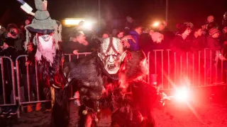 Two individuals in horned costumes are performing in front of a crowd at night, with red lighting illuminating the scene.