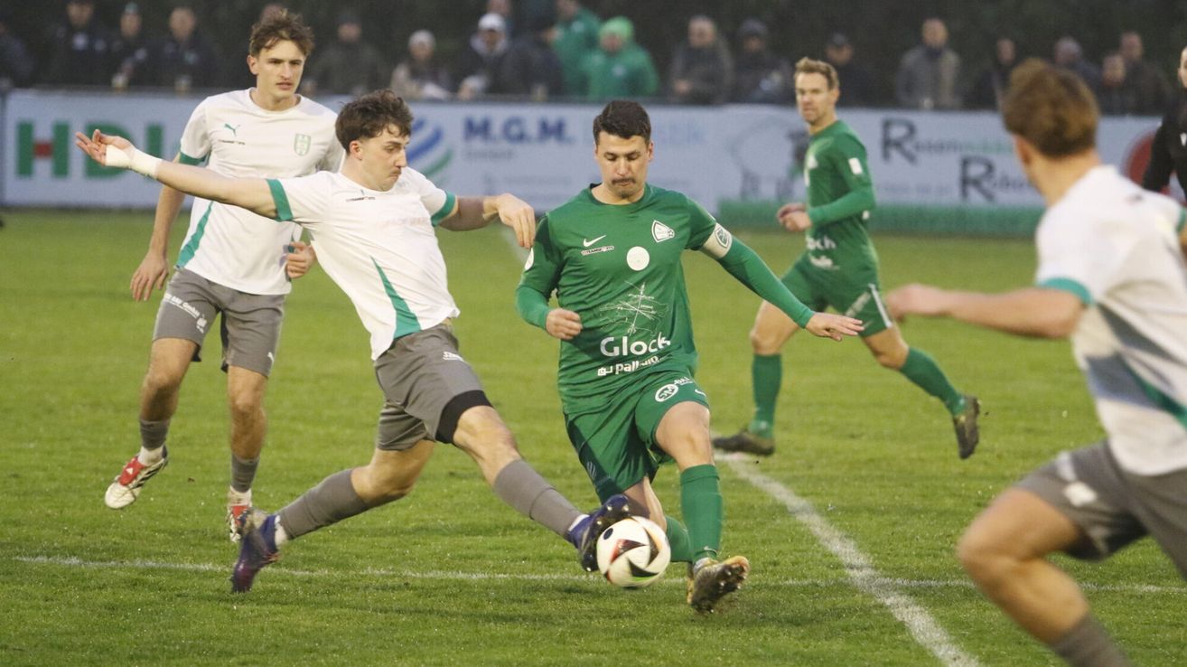 Fußballspieler in grünen und weißen Trikots spielen auf einem Feld. Ein Spieler ist kurz davor, den Ball zu schießen.