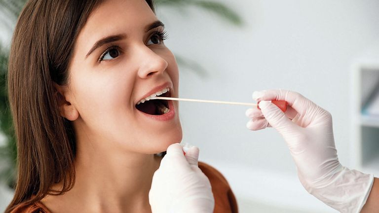 A woman is having a dental examination with a stick in her mouth, wearing white gloves.