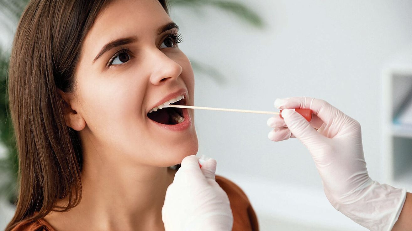 A woman is having a dental examination with a stick in her mouth, wearing white gloves.