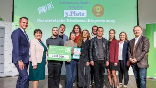 A group of people stand together on a stage, some holding a large green check for EUR 300. They are surrounded by logos and banners.