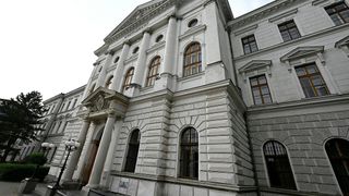 A white neoclassical building with several arched windows and columns. The sign reads 'KREISGERICHT'. A street light is present.