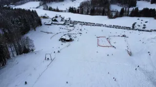 A snowy ski resort with skiers and snowboarders on the slopes, a ski lift, and numerous cars parked around.