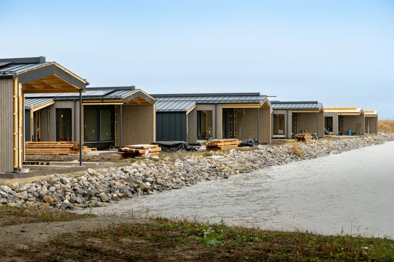 Eine Reihe moderner, hölzerner Häuser im Bau mit Blick auf einen Fluss und einen klaren Himmel.