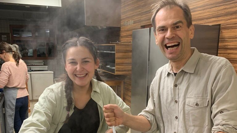 Ein Mann und eine Frau lächeln und posieren für ein Foto in einer Küche mit Holzwänden und einem Kühlschrank.